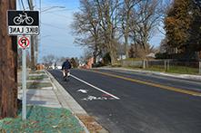 a road with a person riding a bike in the bike lane with a bike lane sign